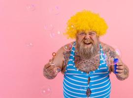förvånad man med gul peruk i huvud spela med bubblor tvål foto
