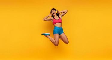 sport kvinna hoppar på en gul bakgrund och lyssna till musik. Lycklig och glad uttryck. foto