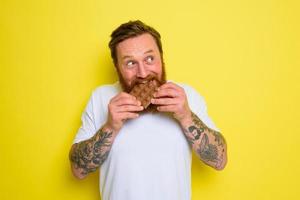 Lycklig man med skägg och tatueringar äter choklad foto