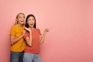 två flickor pekar på något. förvånad uttryck ansikte. rosa bakgrund med tom Plats för din text foto