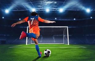 fotboll scen på natt match med spelare i ett orange och blå enhetlig sparkar de straff sparka foto