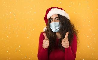 kvinna med jul hatt är optimistisk handla om de nederlag av covid 19 coronavirus. gul bakgrund. foto