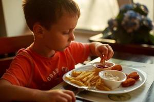 pojke äter snabb mat i en Kafé. de barn äter franska frites med nuggets foto