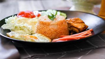 friterad ris, friterad ägg, gurka, skivad tomat, grön sallad och friterad kyckling placerad på en svart tallrik som en garnering. foto