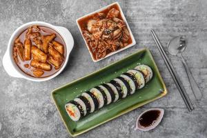 topp se koreanska mat, tteokbokki, kimbap, kimchi med sked och ätpinnar på grå betong tabell. foto