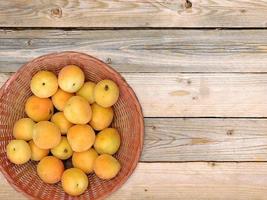 aprikoser i en flätad korg på träbordbakgrund foto