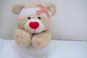 teddy Björn med en sår klänning, sår och bruten händer. sovande i säng. sjukdom av barn foto