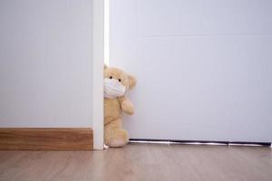 ljus brun söt teddy Björn bär en ansikte mask och en vit dörr inuti de hus. teddy Björn i Hem bakgrund foto