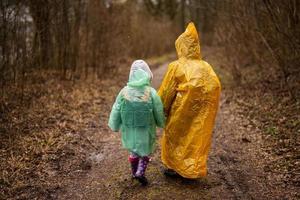 bak- se av bror och syster i regnrockar gående i de skog efter regn. foto