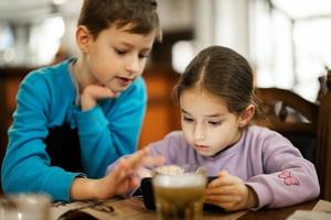 bror med syster spela i smartphone tillsammans, medan äta i restaurang. foto