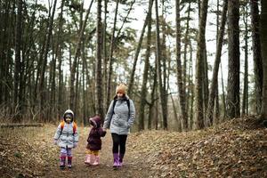 mor och två döttrar med ryggsäckar gående längs de skog väg tillsammans. foto