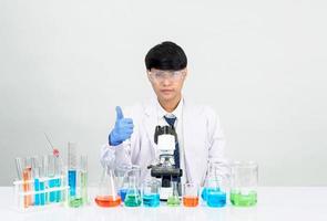 asiatisk manlig studerande forskare i reagens blandning laboratorium i en vetenskap forskning laboratorium med testa rör av olika storlekar och mikroskop. på de tabell i laboratorium kemi labb vit bakgrund. foto