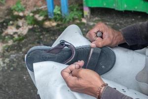 selektiv fokus på sandaler den där är varelse repareras förbi sömnad använder sig av tråd och nålar, detta arbete är kallad i indonesien en tukang sol sepatu, mjuk fokus foto