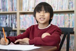 asiatisk pojke skrivning i anteckningsbok, håller på med läxa i en klassrum på skola. utbildning begrepp. foto
