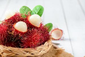 färsk rambutan frukt med löv på bambu korg på trä bakgrund. foto