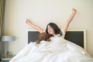 liten asiatisk flicka vaknar upp och stretching på säng i morgon, hälsa vård och Bra morgon- värld foto
