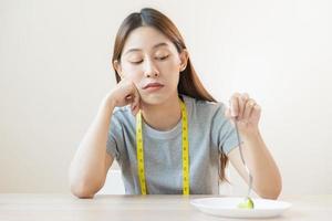 anorexi, olycklig skön asiatisk ung kvinna, flicka på bantning, hand innehav gaffel på broccoli i sallad tallrik, motvilja eller trött med äta färsk grönsaker. näring av rena, friska mat Bra smak. foto