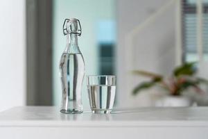 en glas av rena dricka vatten och en vatten flaska på en vit trä- tabell foto