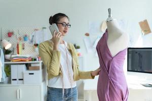 designer flicka bär glasögon talande på de telefon och granskning de design av de kläder. foto