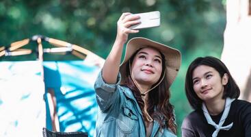 asiatisk Söt kvinna och flickvän använda sig av smartphone selfie på camping foto