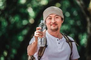 porträtt asiatisk resande man med ryggsäck som visar vatten flaska foto