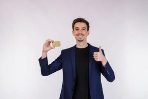 porträtt av ung leende stilig affärsman som visar kreditera kort och tumme upp isolerat över vit bakgrund foto