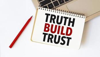 bärbar dator, röd penna och anteckningsblock med text sanning bygga förtroende i de vit bakgrund foto