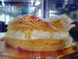 klassisk efterrätt jätte ringar av paris-brest choux bakverk, creme mousseline, fylld med mjuk ost grädde pulveriserad med socker pulver, tjock vaniljsås kaka i mörk bakgrund foto