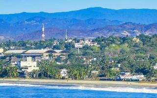 Sol strand klippor stenar vågor palmer bergen puerto escondido Mexiko. foto