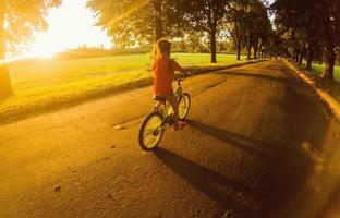 liten flicka med ridning cykel på solnedgång foto