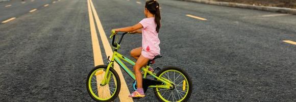 barn inlärning till kör en cykel på en uppfart utanför. liten flickor ridning Cyklar på asfalt väg i de stad bär hjälmar som skyddande redskap. foto