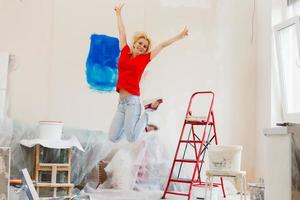 ung skön kvinna hoppa och målarfärger de vägg och vit måla vält foto