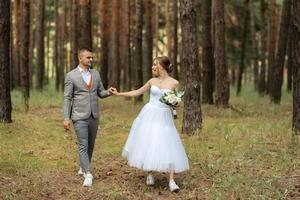 ung par brud i en vit kort klänning och brudgum i en grå kostym i en tall skog foto
