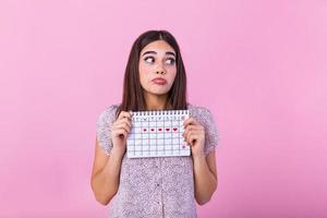 porträtt av ung kvinna i klänning, innehav kvinna perioder kalender för kontroll menstruation dagar isolerat på trender rosa bakgrund. medicinsk sjukvård, gynekologisk begrepp. foto