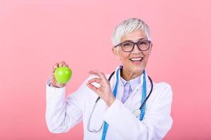 leende mogna dietist innehav en frukt och som visar friska saftig äpple. läkare eller dietist håll ett äpple. Bra medicinsk sjukvård näring begrepp. ett äpple en dag håller de läkare bort foto