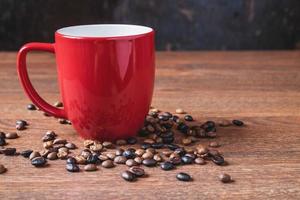 kaffe i en röd kaffekopp bredvid spillda kaffebönor på ett träbord