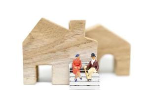 miniatyr man och hustru som sitter framför ett hus på en vit bakgrund, familjekoncept foto