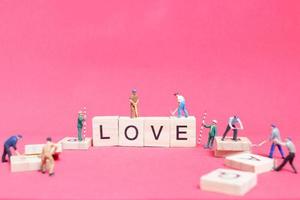 miniatyrarbetare som bygger ordet kärlek på träklossar med rosa bakgrund, alla hjärtans dagskoncept foto