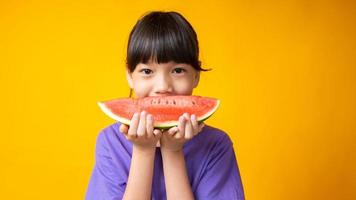 ung asiatisk tjej som ler i purpur skjortainnehavskiva vattenmelon i studio med gul bakgrund