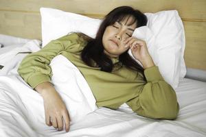 en ledsen ung asiatisk kvinna är gråt medan liggande på de säng foto
