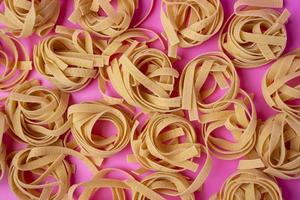 en mönster av rå tagliatelle på en rosa bakgrund, pasta bon, ägg klistra foto