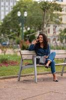 ung afrikansk amerikan affärskvinna talande på de telefon Sammanträde på de bänk i de stad parkera foto