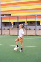 en Tonårs pojke står på en grön fält i de skola gård med en fotboll boll foto