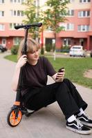 en Tonårs flicka är Sammanträde på en skoter med en telefon och leende. virtuell kommunikation foto