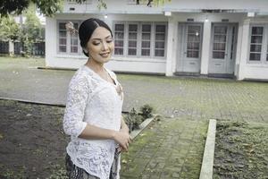 en ung indonesiska kvinna med en Lycklig framgångsrik uttryck bär en vit kebaya. kartinis dag begrepp. foto