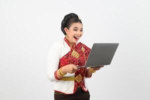 porträtt av skön thai kvinna i traditionell Kläder Framställ med bärbar dator dator foto