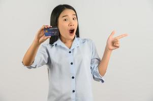 porträtt av positiv ung asiatisk kvinna som visar kreditera kort Bra humör lön och pekande finger på åt sidan isolerat på vit bakgrund foto