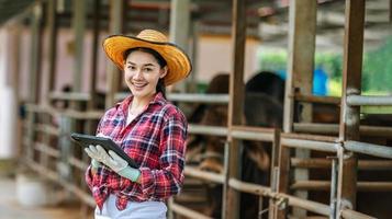 Lycklig asiatisk ung jordbrukare kvinna med läsplatta pc dator medan stående och ser på kamera på mejeri odla. lantbruk industri, jordbruk, människor, teknologi och djur- hushållning begrepp. foto