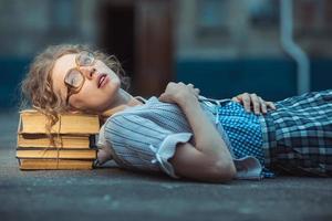 rolig galen flicka studerande med glasögon liggande på en lugg av böcker foto