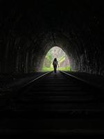 flicka gående genom en mörk tunnel till de utgång. ljus på de slutet av de tunnel, utgång från de mörk järnväg tunnel foto